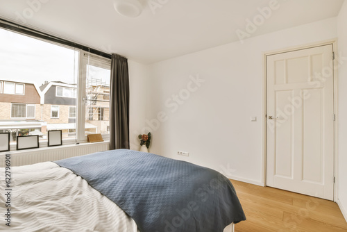a bedroom with white walls and hardwood flooring the room has a large window that looks out onto the street