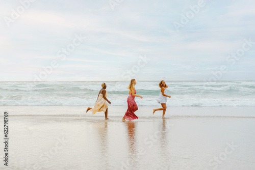 multiracial group of three young women running along the shore on the beach. friends enjoying their summer vacation together on the coast. friendship and unity.