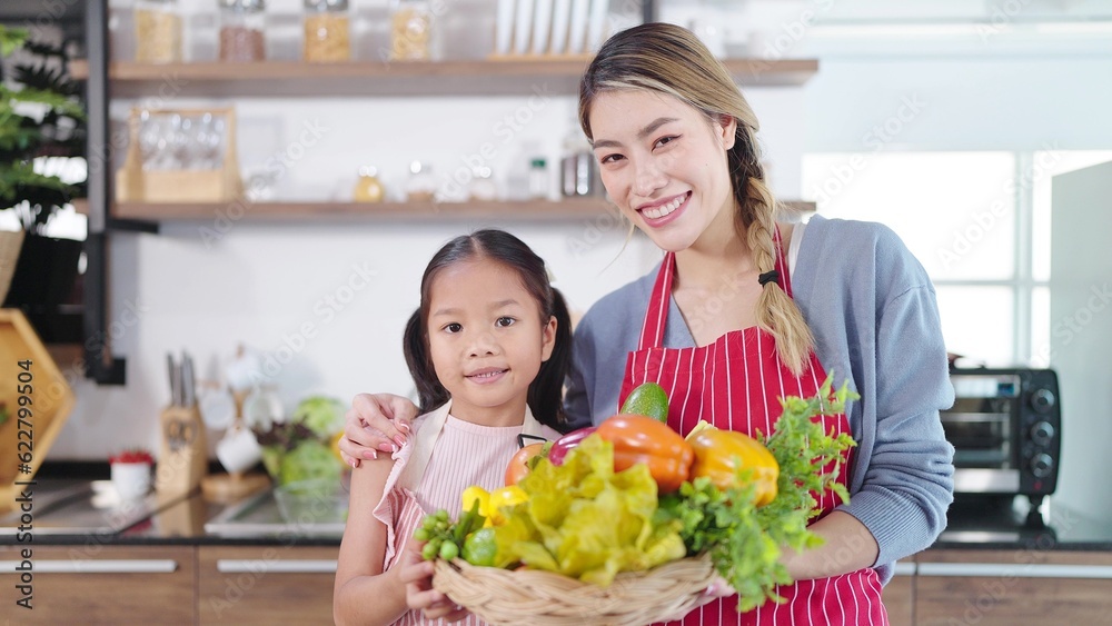 Portrait of asian mother and little daughter holding vegetables basket smiling and looking at camera. Happy family, Healthy food, Single mom concept