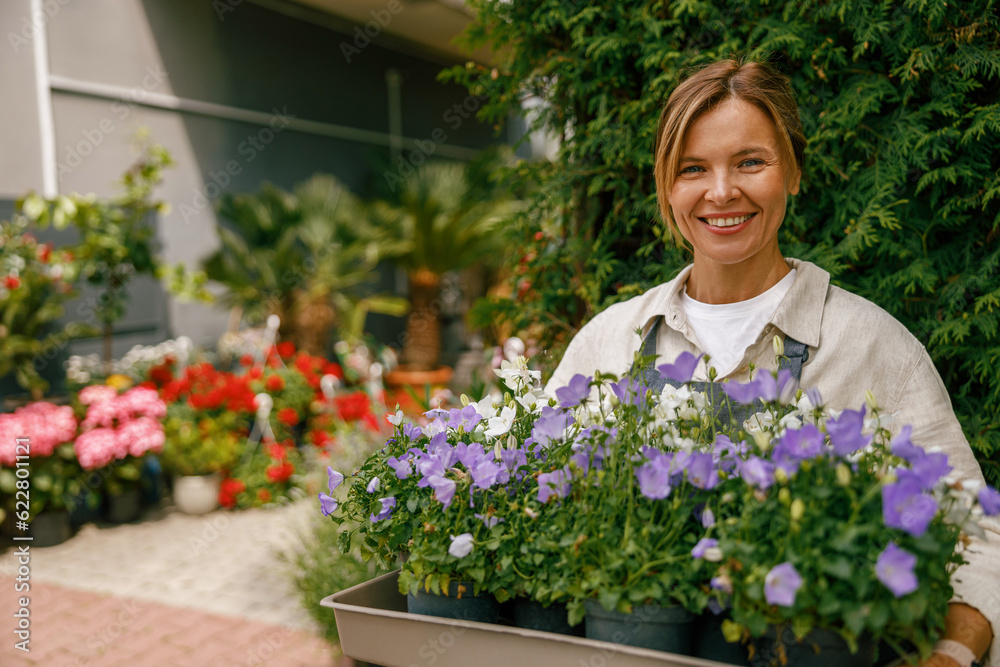 Woman florist small business owner standing in floral store and waiting for client with houseplants