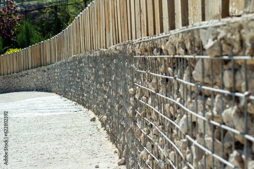 Fence made of mesh and stone with wooden planks