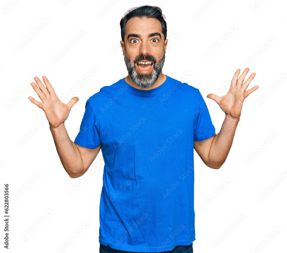Middle aged man with beard wearing casual blue t shirt celebrating crazy and amazed for success with arms raised and open eyes screaming excited. winner concept Middle aged man with beard wearing casual blue t shirt celebrating crazy and amazed for success with arms raised and open eyes screaming excited. winner concept