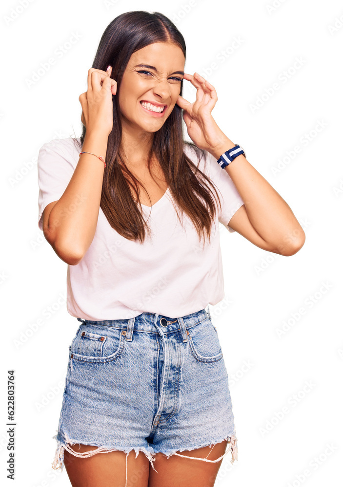 Young hispanic woman wearing casual white tshirt covering ears with fingers with annoyed expression for the noise of loud music. deaf concept. Young hispanic woman wearing casual white tshirt covering ears with fingers with annoyed expression for the noise of loud music. deaf concept.