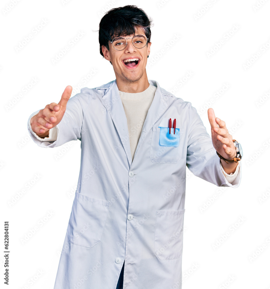 Handsome hipster young man wearing doctor uniform looking at the camera smiling with open arms for hug. cheerful expression embracing happiness. Handsome hipster young man wearing doctor uniform looking at the camera smiling with open arms for hug. cheerful expression embracing happiness.