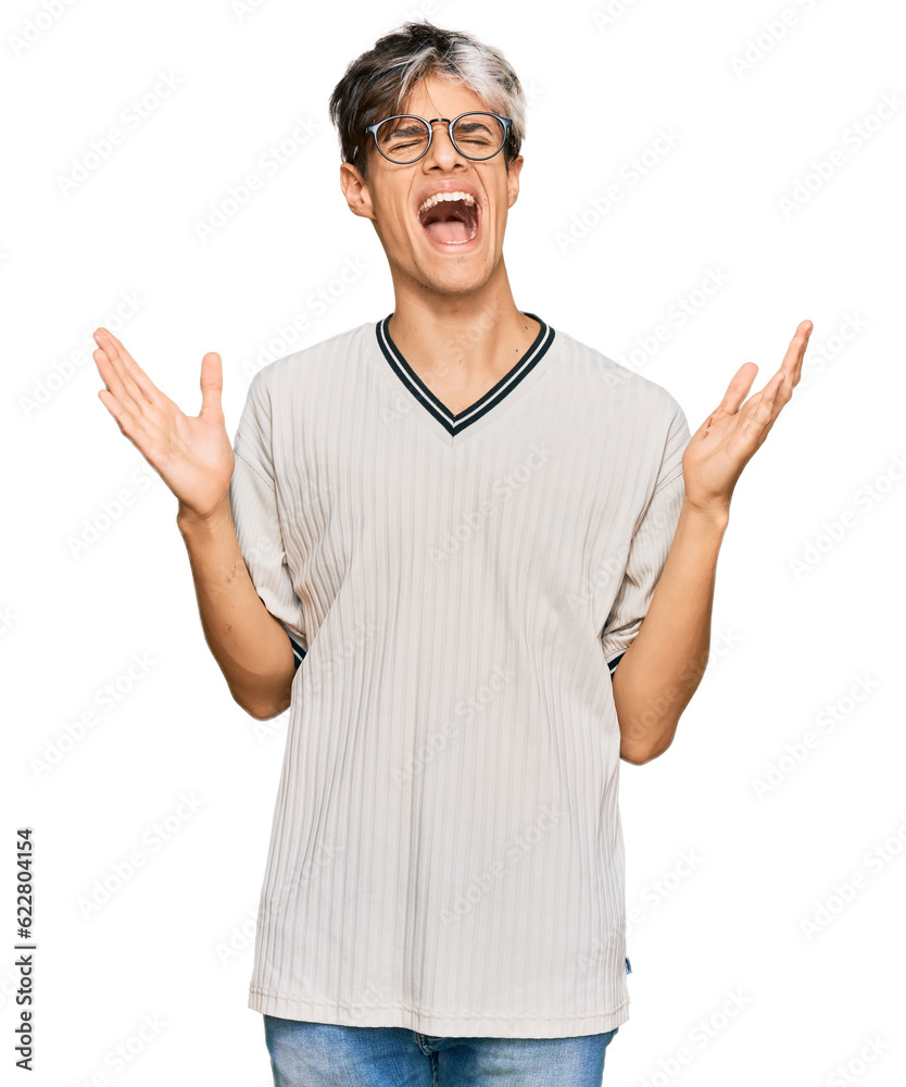 Naklejka premium Young hispanic man wearing casual clothes and glasses celebrating mad and crazy for success with arms raised and closed eyes screaming excited. winner concept