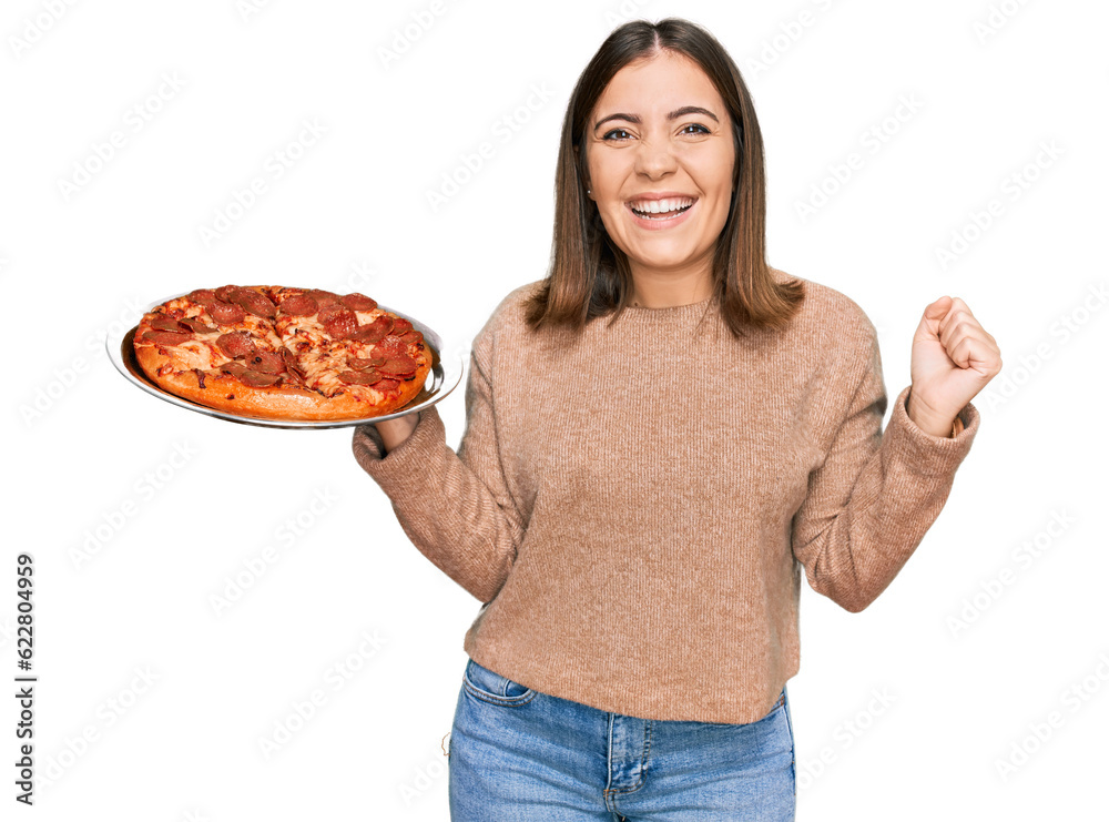 Young beautiful woman holding italian pizza screaming proud, celebrating victory and success very excited with raised arms Young beautiful woman holding italian pizza screaming proud, celebrating victory and success very excited with raised arms