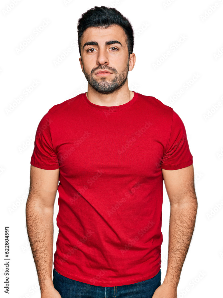 Hispanic man with beard wearing casual red t shirt relaxed with serious expression on face. simple and natural looking at the camera. Hispanic man with beard wearing casual red t shirt relaxed with serious expression on face. simple and natural looking at the camera.