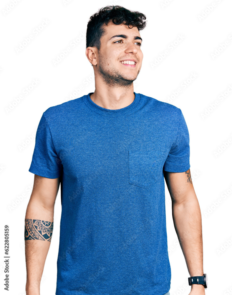 Fototapeta premium Young hispanic man wearing casual t shirt looking away to side with smile on face, natural expression. laughing confident.