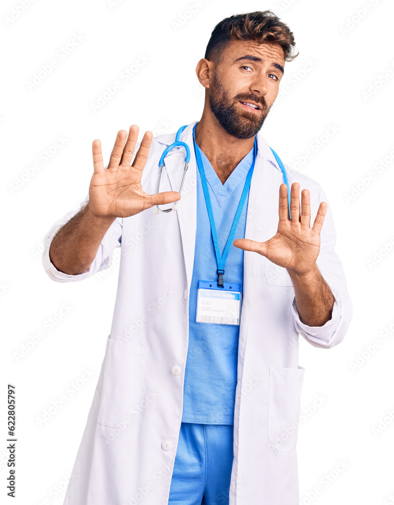 Young hispanic man wearing doctor uniform and stethoscope afraid and terrified with fear expression stop gesture with hands, shouting in shock. panic concept. Young hispanic man wearing doctor uniform and stethoscope afraid and terrified with fear expression stop gesture with hands, shouting in shock. panic concept.