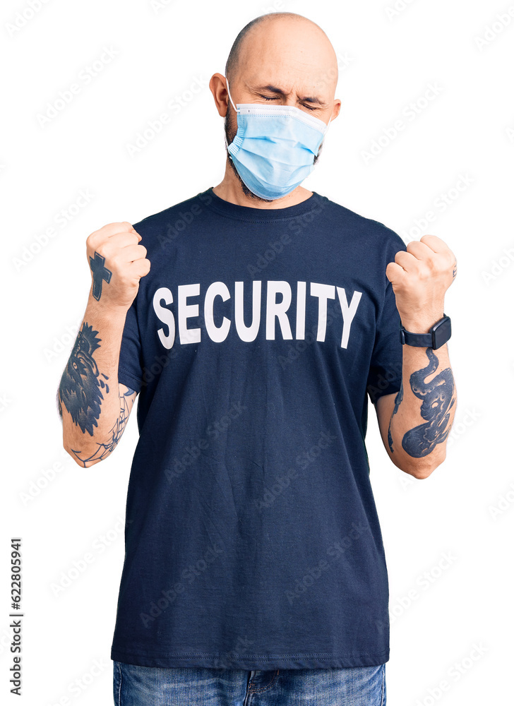 Young handsome man wearing security t shirt and medical mask very happy and excited doing winner gesture with arms raised, smiling and screaming for success. celebration concept. Young handsome man wearing security t shirt and medical mask very happy and excited doing winner gesture with arms raised, smiling and screaming for success. celebration concept.