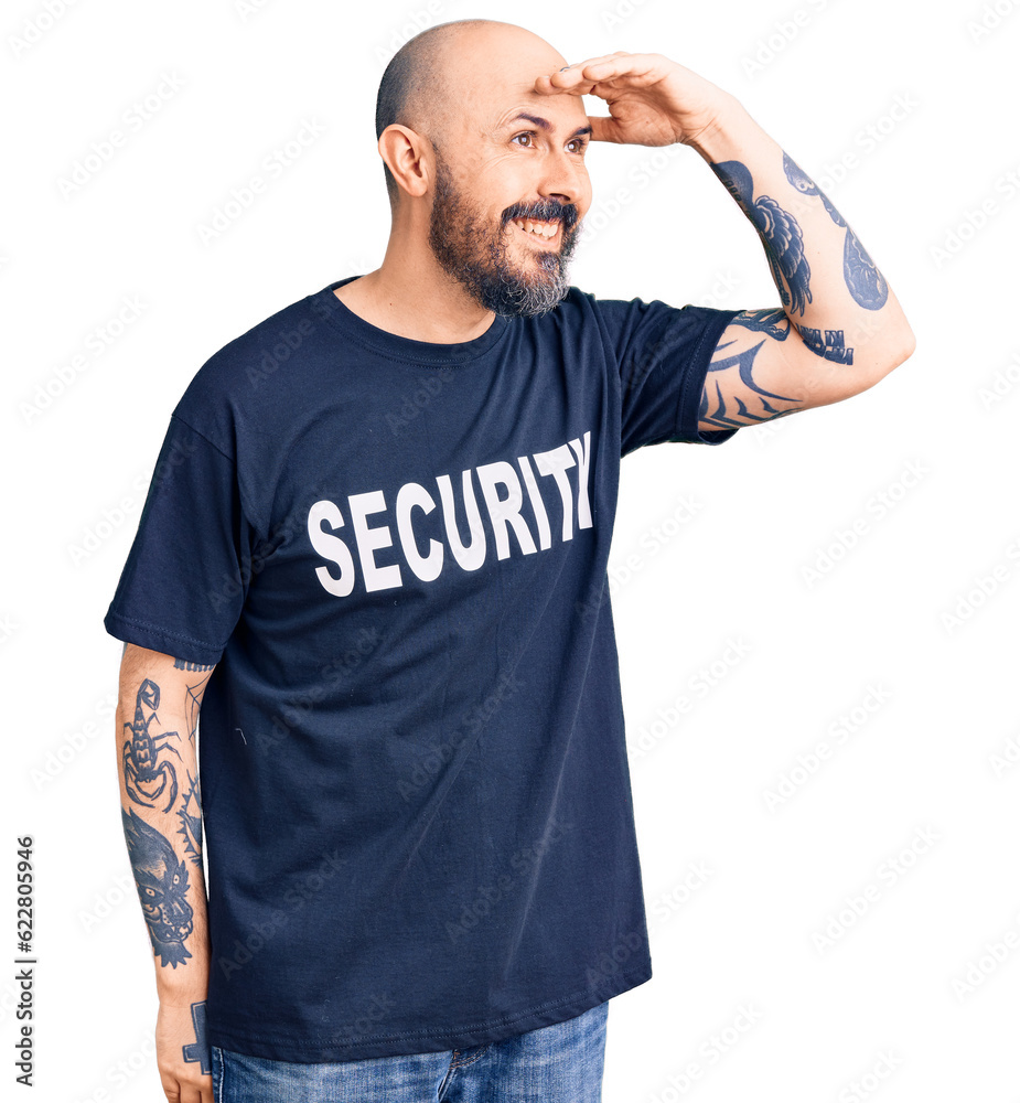 Young handsome man wearing security t shirt very happy and smiling looking far away with hand over head. searching concept. Young handsome man wearing security t shirt very happy and smiling looking far away with hand over head. searching concept.