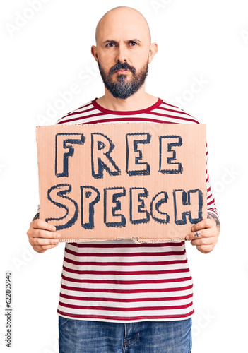 Young handsome man holding free speech banner thinking attitude and sober expression looking self confident