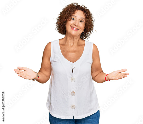 Beautiful middle age mature woman wearing casual white shirt clueless and confused expression with arms and hands raised. doubt concept.
