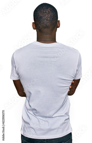 Young african american man wearing casual white t shirt standing backwards looking away with crossed arms photo