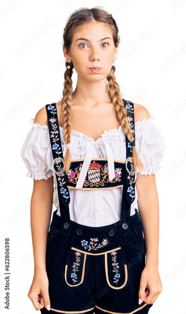 Beautiful caucasian woman with blonde hair wearing octoberfest traditional clothes puffing cheeks with funny face. mouth inflated with air, crazy expression. Beautiful caucasian woman with blonde hair wearing octoberfest traditional clothes puffing cheeks with funny face. mouth inflated with air, crazy expression.