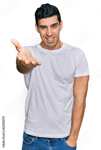 Handsome hispanic man wearing casual white t shirt smiling friendly offering handshake as greeting and welcoming. successful business.
