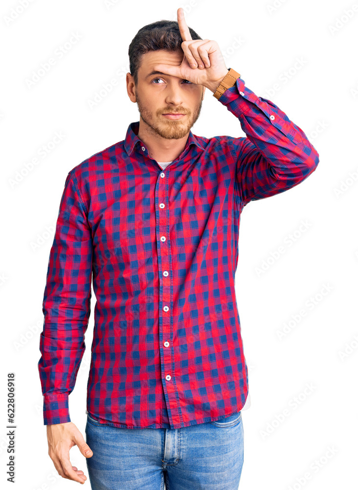 Handsome young man with bear wearing casual shirt making fun of people with fingers on forehead doing loser gesture mocking and insulting. Handsome young man with bear wearing casual shirt making fun of people with fingers on forehead doing loser gesture mocking and insulting.