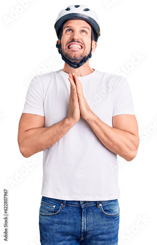 Young handsome man wearing bike helmet begging and praying with hands together with hope expression on face very emotional and worried. begging.