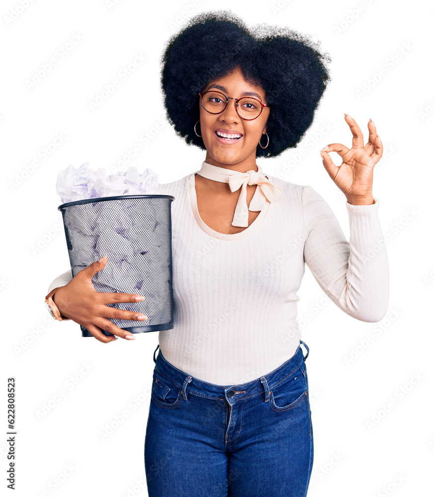 Young african american girl holding paper bin full of crumpled papers doing ok sign with fingers, smiling friendly gesturing excellent symbol Young african american girl holding paper bin full of crumpled papers doing ok sign with fingers, smiling friendly gesturing excellent symbol