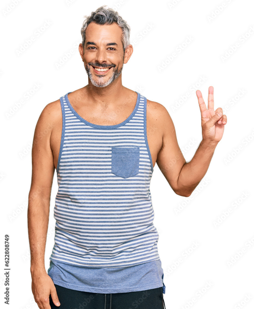 Middle age grey-haired man wearing casual style with sleeveless shirt smiling with happy face winking at the camera doing victory sign. number two. Middle age grey-haired man wearing casual style with sleeveless shirt smiling with happy face winking at the camera doing victory sign. number two.