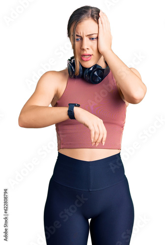 Beautiful caucasian young woman wearing gym clothes and using headphones looking at the watch time worried, afraid of getting late