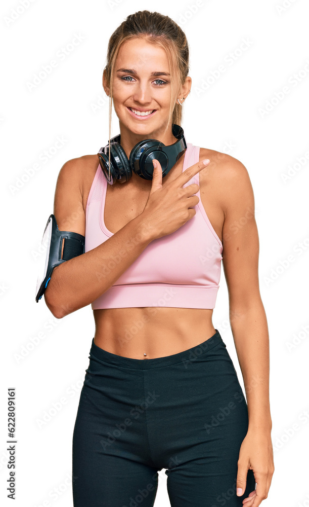 Young blonde woman wearing gym clothes and using headphones cheerful with a smile of face pointing with hand and finger up to the side with happy and natural expression on face Young blonde woman wearing gym clothes and using headphones cheerful with a smile of face pointing with hand and finger up to the side with happy and natural expression on face