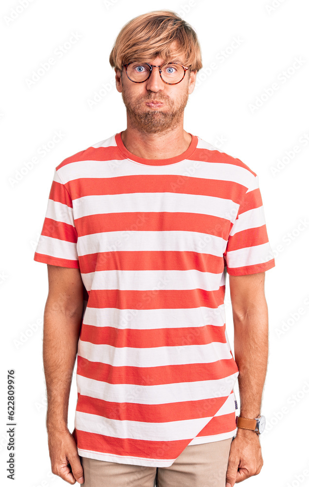 Handsome caucasian man with beard wearing casual clothes and glasses puffing cheeks with funny face. mouth inflated with air, crazy expression. Handsome caucasian man with beard wearing casual clothes and glasses puffing cheeks with funny face. mouth inflated with air, crazy expression.