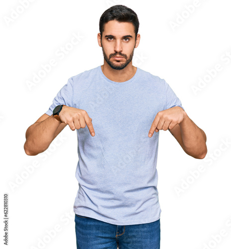 Young hispanic man wearing casual clothes pointing down looking sad and upset, indicating direction with fingers, unhappy and depressed.