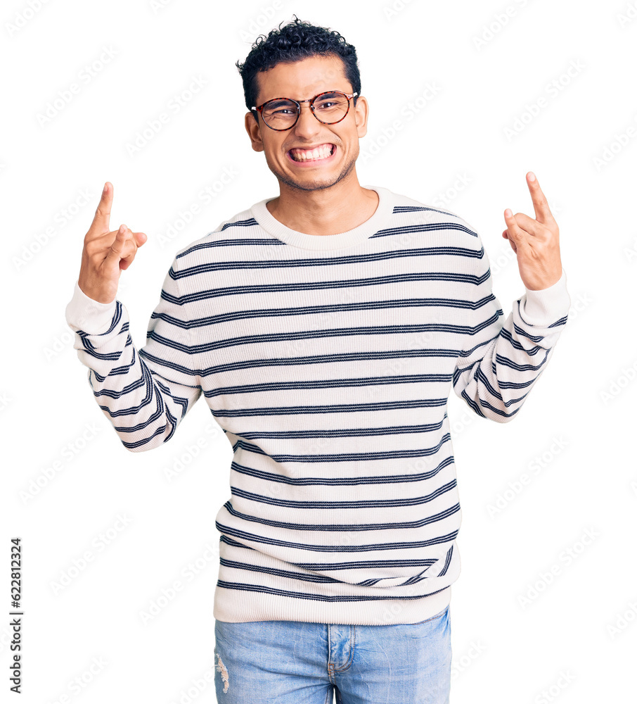 Hispanic handsome young man wearing casual clothes and glasses shouting with crazy expression doing rock symbol with hands up. music star. heavy concept. Hispanic handsome young man wearing casual clothes and glasses shouting with crazy expression doing rock symbol with hands up. music star. heavy concept.