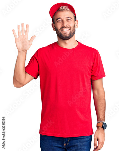 Young handsome blond man wearing t-shirt and cap showing and pointing up with fingers number five while smiling confident and happy.