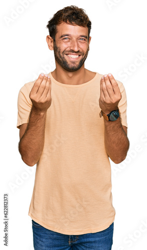 Handsome young man with beard wearing casual tshirt doing money gesture with hands, asking for salary payment, millionaire business