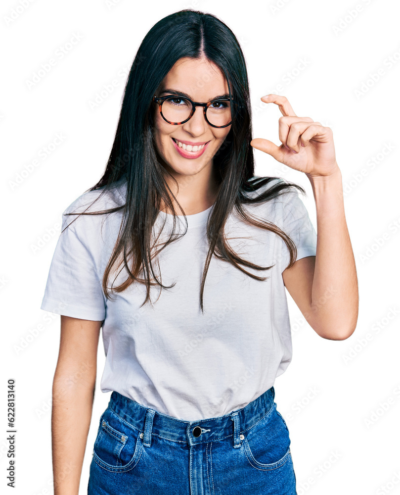 Young hispanic woman wearing casual clothes and glasses smiling and confident gesturing with hand doing small size sign with fingers looking and the camera. measure concept. Young hispanic woman wearing casual clothes and glasses smiling and confident gesturing with hand doing small size sign with fingers looking and the camera. measure concept.