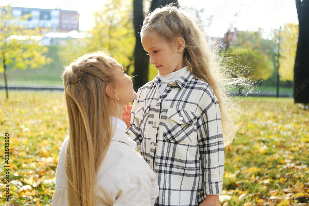 Fototapeta premium Mother and daughter spend time together in the autumn park. Mother lovingly looks at her daughter