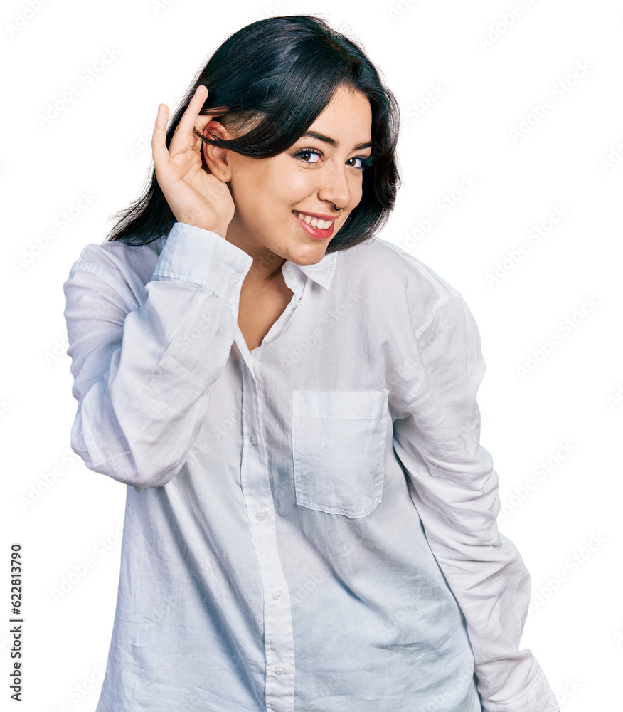 Beautiful hispanic woman wearing casual white shirt smiling with hand over ear listening an hearing to rumor or gossip. deafness concept. Beautiful hispanic woman wearing casual white shirt smiling with hand over ear listening an hearing to rumor or gossip. deafness concept.