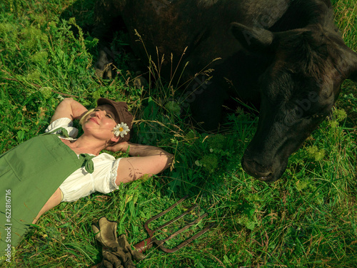 blonde with a short haircut in a green jumpsuit in nature with a black cow