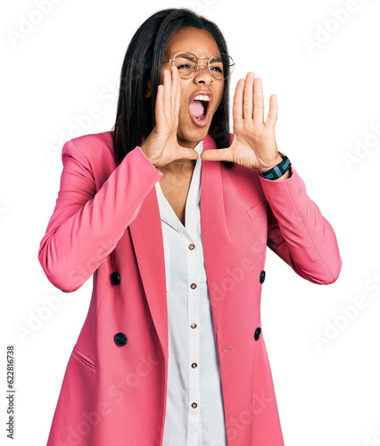 Beautiful hispanic woman wearing business jacket shouting angry out loud with hands over mouth