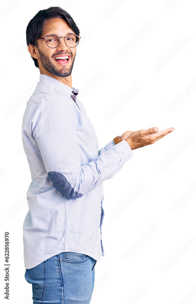 Handsome hispanic man wearing business shirt and glasses pointing aside with hands open palms showing copy space, presenting advertisement smiling excited happy Handsome hispanic man wearing business shirt and glasses pointing aside with hands open palms showing copy space, presenting advertisement smiling excited happy