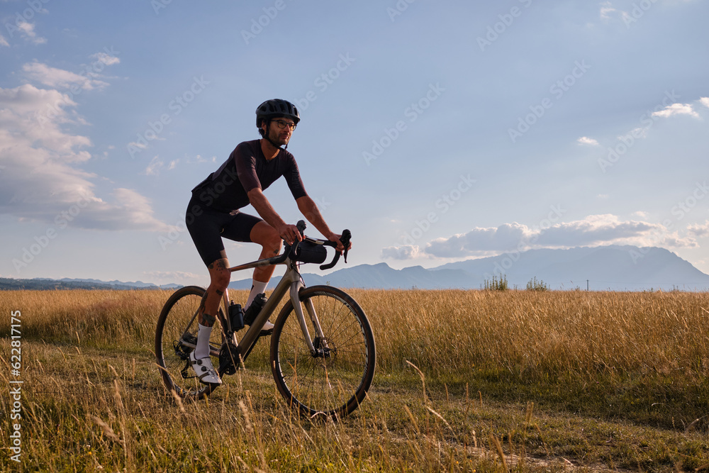 Male cyclist wearing cycling kit and helmet riding on the road a gravel bike at sunset.Sports motivation image. Male cyclist wearing cycling kit and helmet riding on the road a gravel bike at sunset.Sports motivation image.