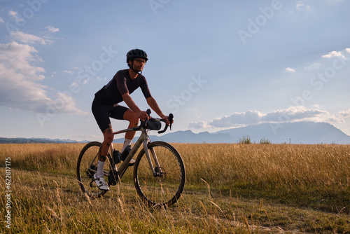 Male cyclist wearing cycling kit and helmet riding on the road a gravel bike at sunset.Sports motivation image. © Ketrin