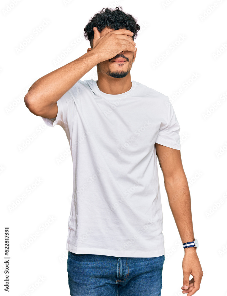 Young arab man wearing casual white t shirt covering eyes with hand, looking serious and sad. sightless, hiding and rejection concept Young arab man wearing casual white t shirt covering eyes with hand, looking serious and sad. sightless, hiding and rejection concept
