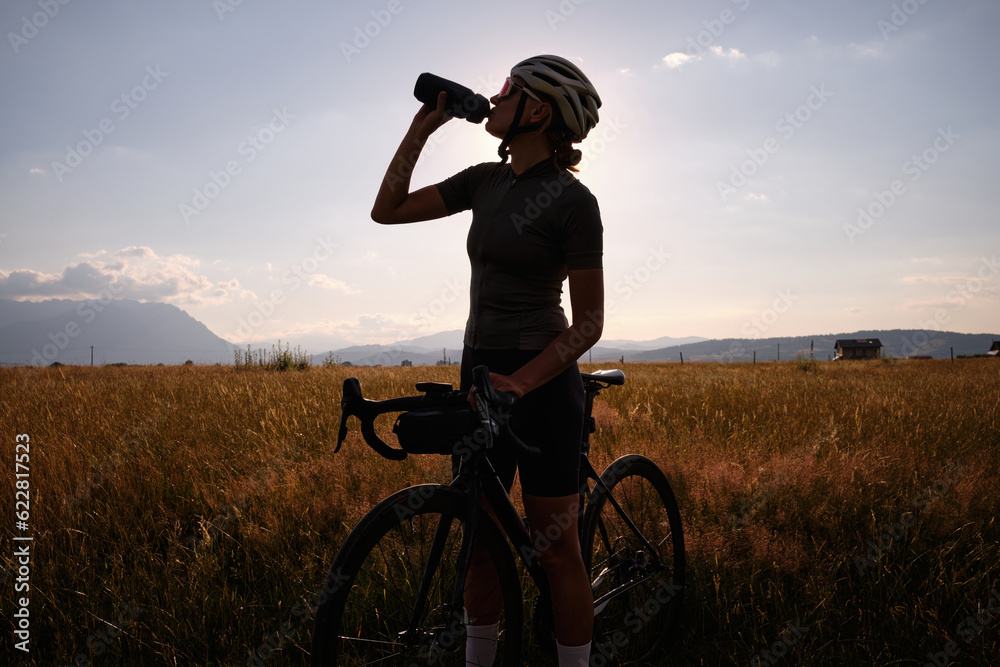Female cyclist in cycling clothes and a helmet drinks water from a sports bottle. Female cyclist in cycling clothes and a helmet drinks water from a sports bottle.