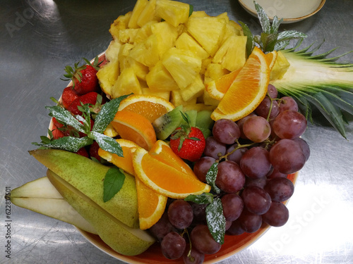 fresh and ripe fruits and berries on a large plate before serving. pineapple  grapes  orange  strawberry and pear are a delicious and healthy dessert for children and adults