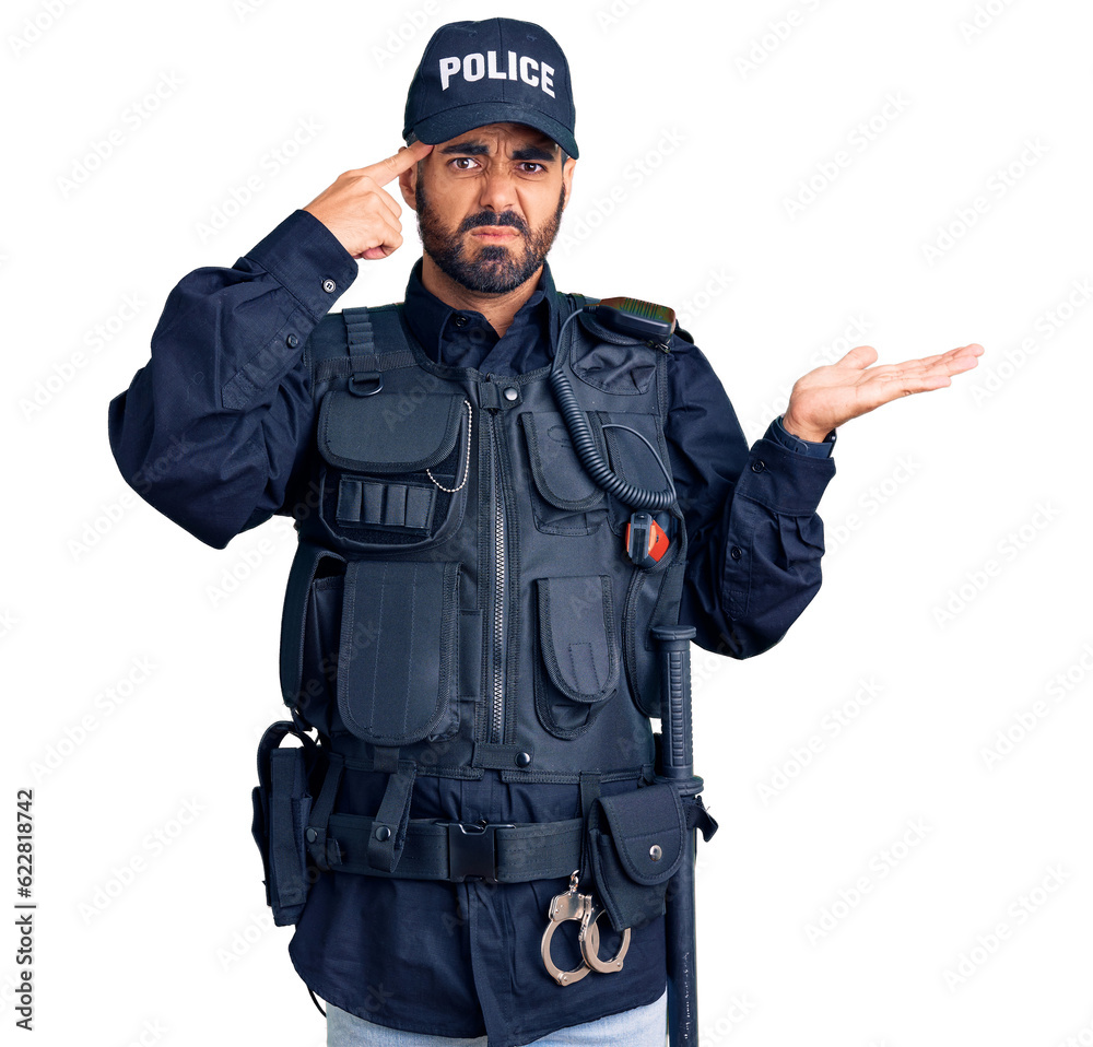 Young hispanic man wearing police uniform confused and annoyed with open palm showing copy space and pointing finger to forehead. think about it.