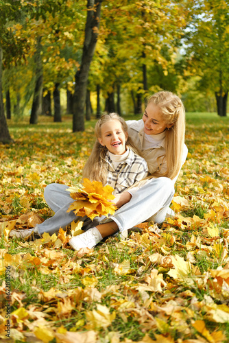 The family has fun in the park. Girl and mother sit on the ground among yellow leaves and fool around