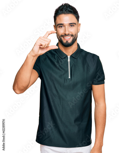 Young man with beard wearing sportswear smiling and confident gesturing with hand doing small size sign with fingers looking and the camera. measure concept.