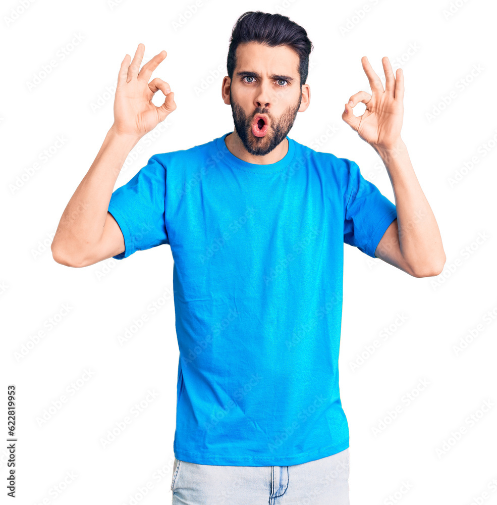 Young handsome man with beard wearing casual t-shirt looking surprised and shocked doing ok approval symbol with fingers. crazy expression Young handsome man with beard wearing casual t-shirt looking surprised and shocked doing ok approval symbol with fingers. crazy expression