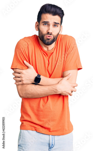 Young handsome man with beard wearing casual t-shirt shaking and freezing for winter cold with sad and shock expression on face