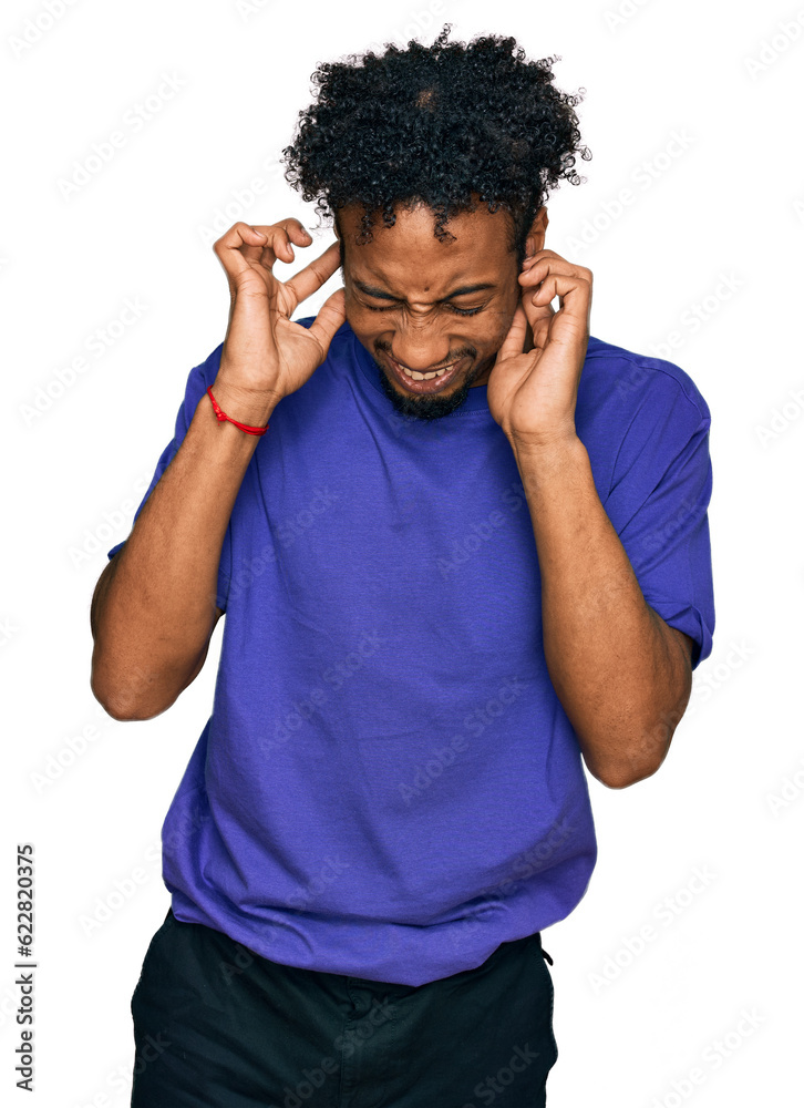 Young african american man with beard wearing casual purple t shirt covering ears with fingers with annoyed expression for the noise of loud music. deaf concept. Young african american man with beard wearing casual purple t shirt covering ears with fingers with annoyed expression for the noise of loud music. deaf concept.