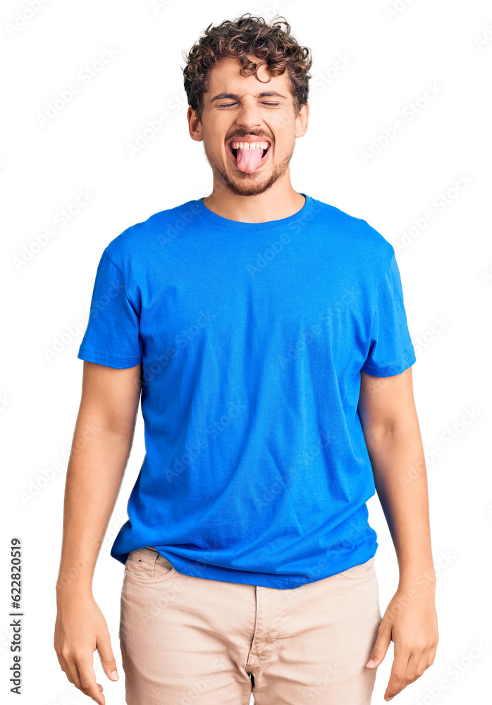 Obraz premium Young handsome man with curly hair wearing casual clothes sticking tongue out happy with funny expression. emotion concept.