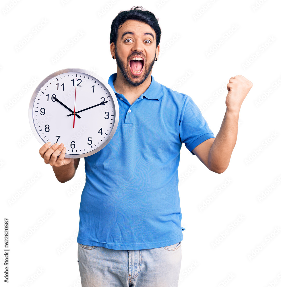 Young hispanic man holding big clock screaming proud, celebrating victory and success very excited with raised arms Young hispanic man holding big clock screaming proud, celebrating victory and success very excited with raised arms